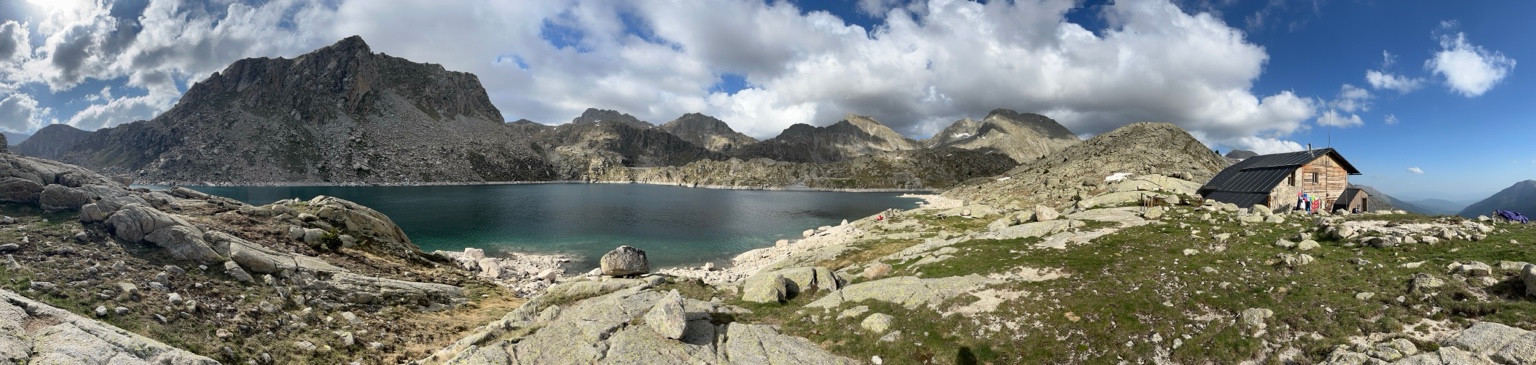 Colomina refuge at the right of a wide panorama of a rocky mountain lake