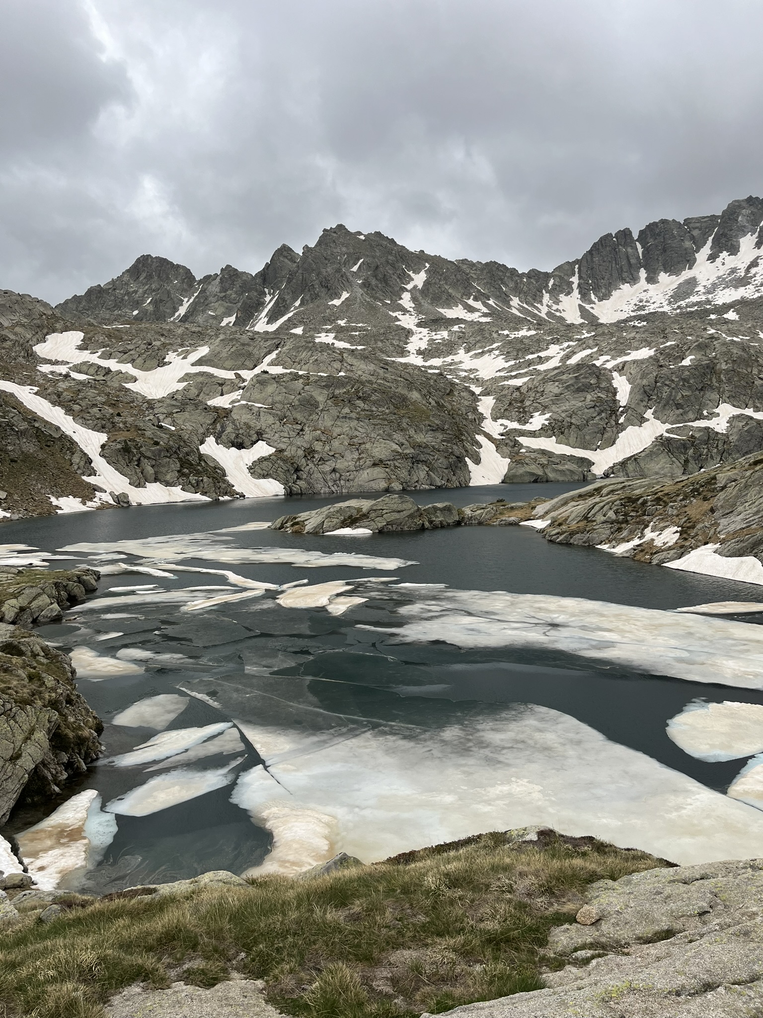 Broken ice on a mountain lake surrounded by granite and patches of snow