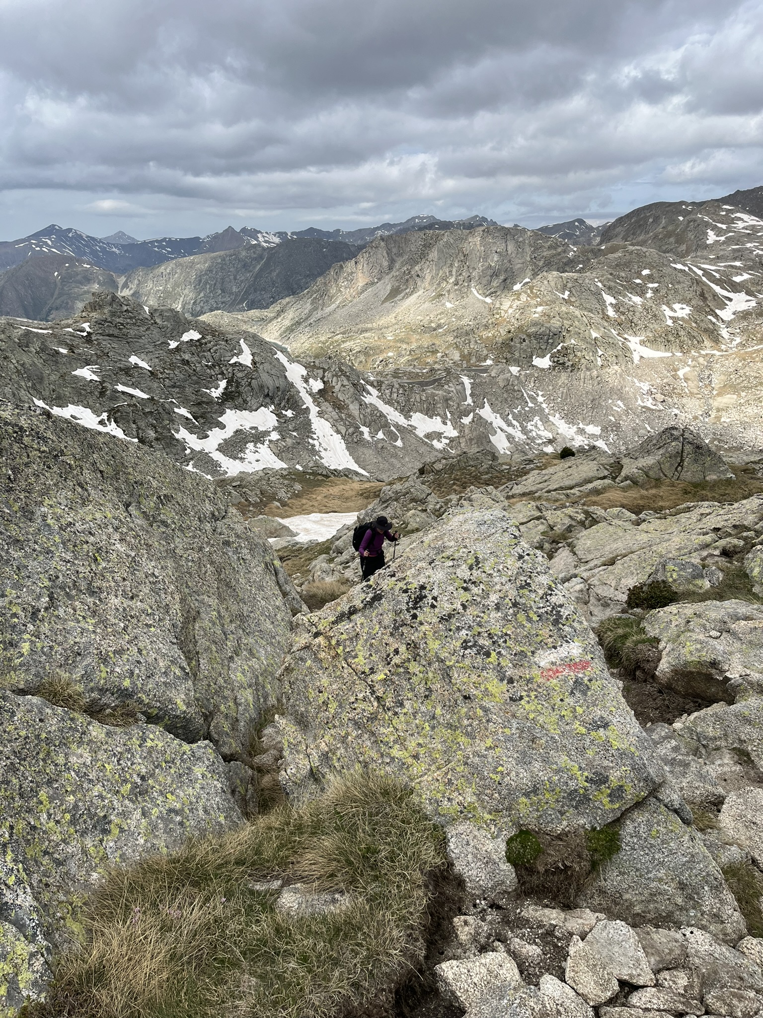 A walker among granite boulders beneath snow-patched mountain slopes