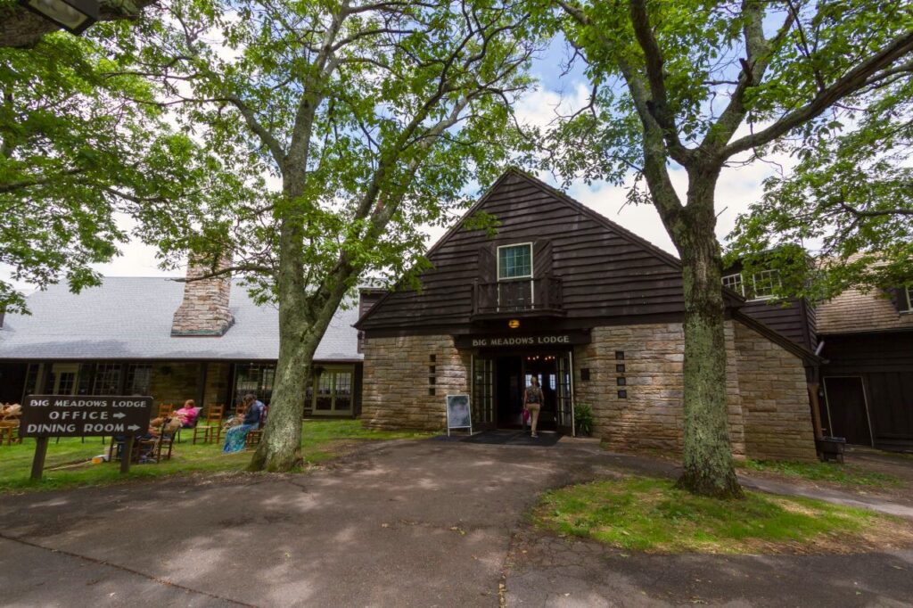 The stone and timber entrance of Big Meadows Lodge among leafy trees.