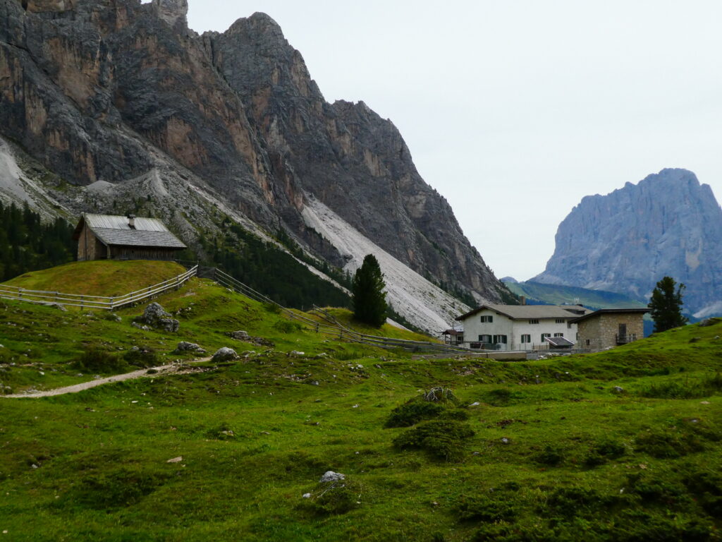 Rifugio Firenze and a small wooden building in green meadows beneath tall rock walls