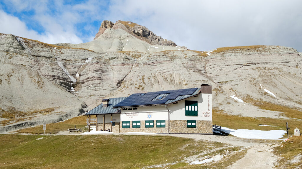 White Rifugio Puez with green shutters below pale limestone slopes